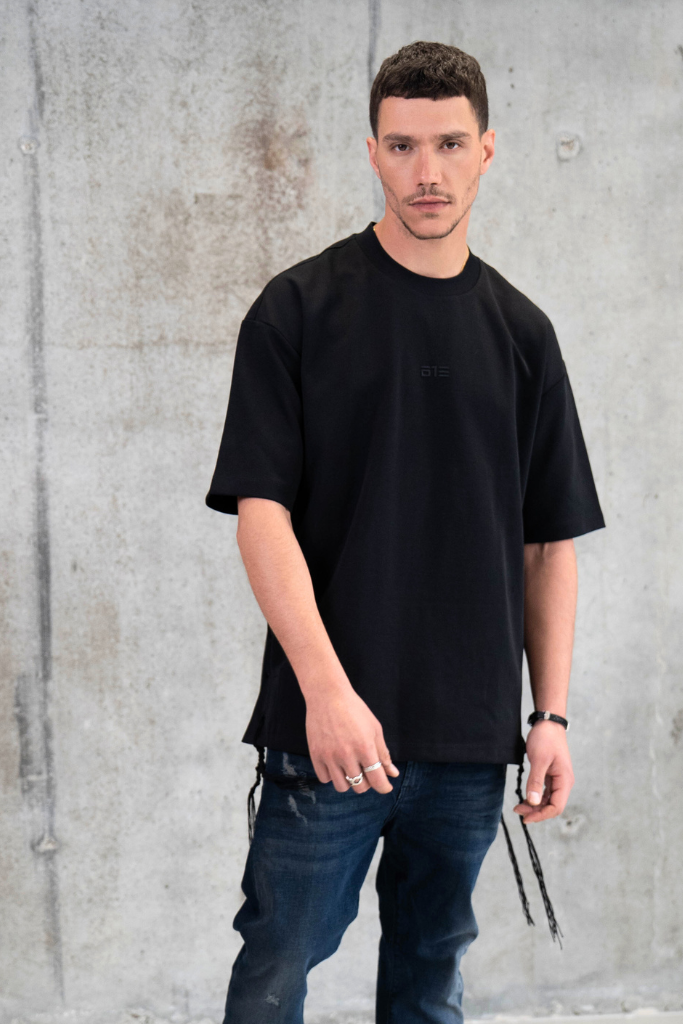 חולצת ציצית שחורה דגם PURE TEXTURE על הדוגמן בצילומי סטודיו עם רקע בטון