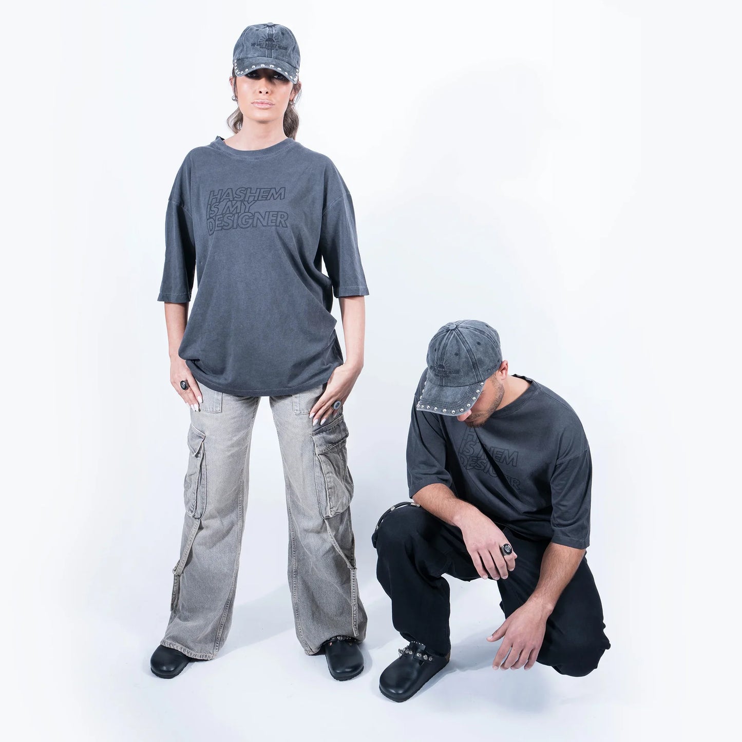 טישרט אפורה הדפס "HASHEM IS MY DESIGNER" על דוגמן יושב ודוגמנית עומדת בצילומי סטודיו - פרונט